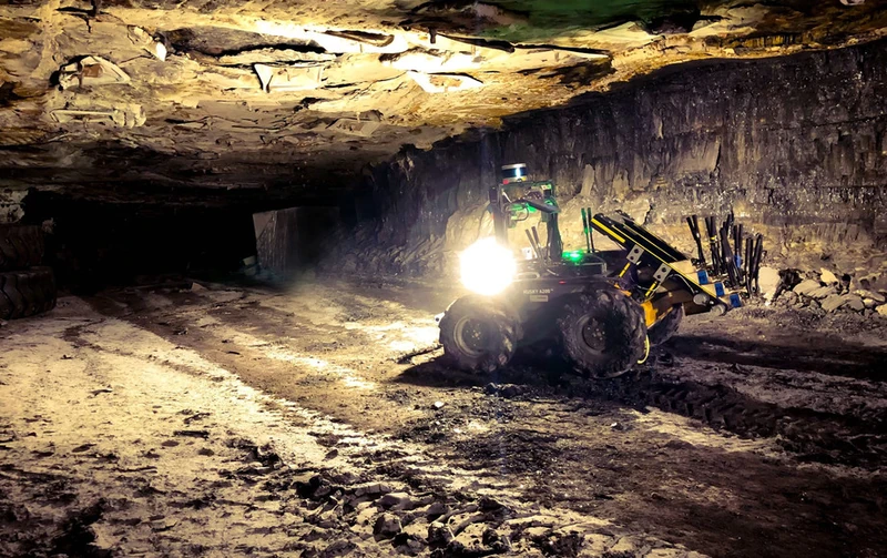 A robot traversing loose rubble in an unlit underground mine passage.